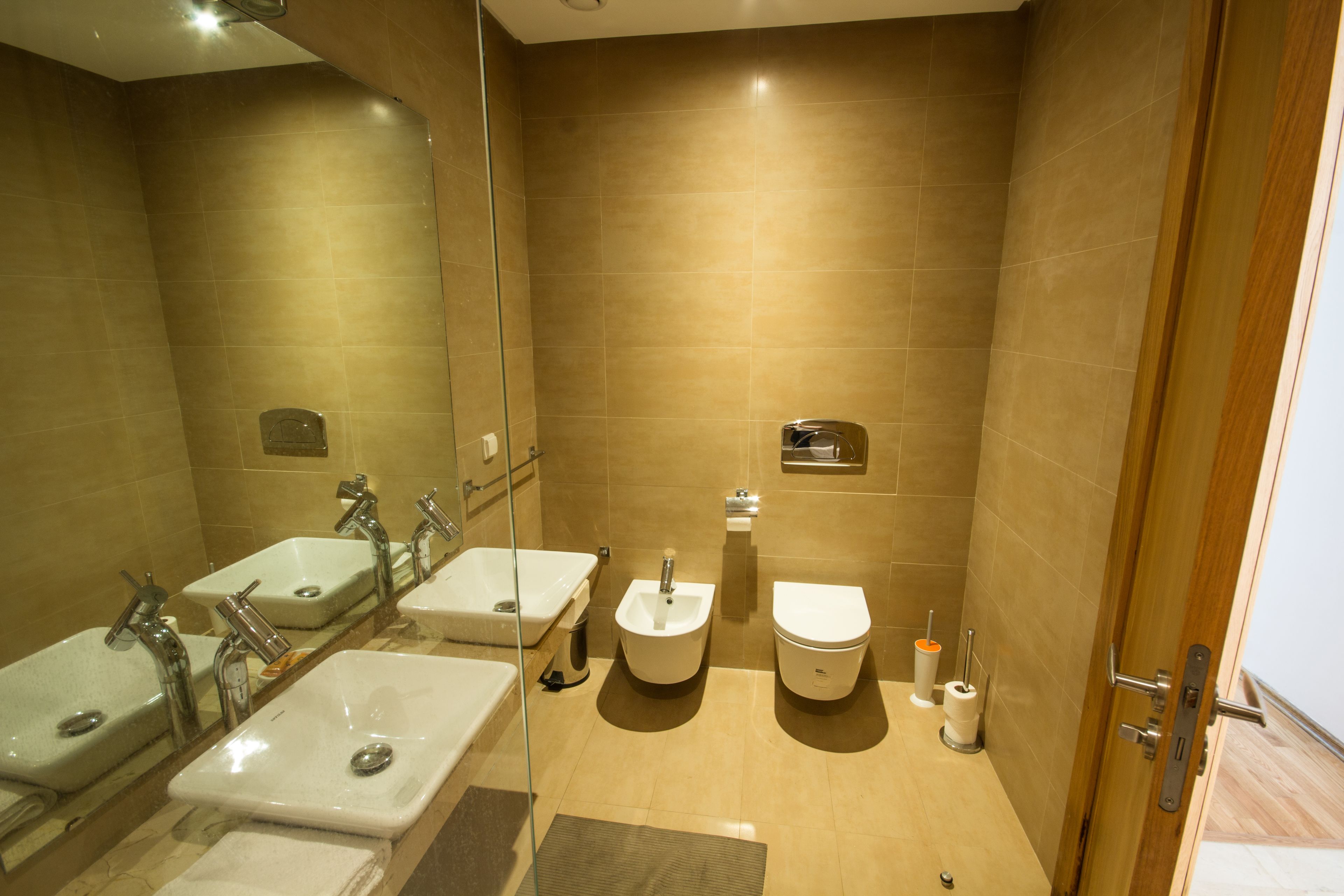 A modern bathroom with three sinks, a bidet, and a toilet.