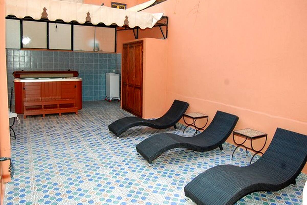 Un solarium con suelo de baldosas, un banco de madera, una mesita y dos sillones.