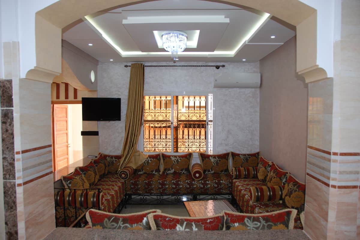 Amplia sala de estar con un conjunto de sofás, una televisión y un ventanal decorativo con celosías.
