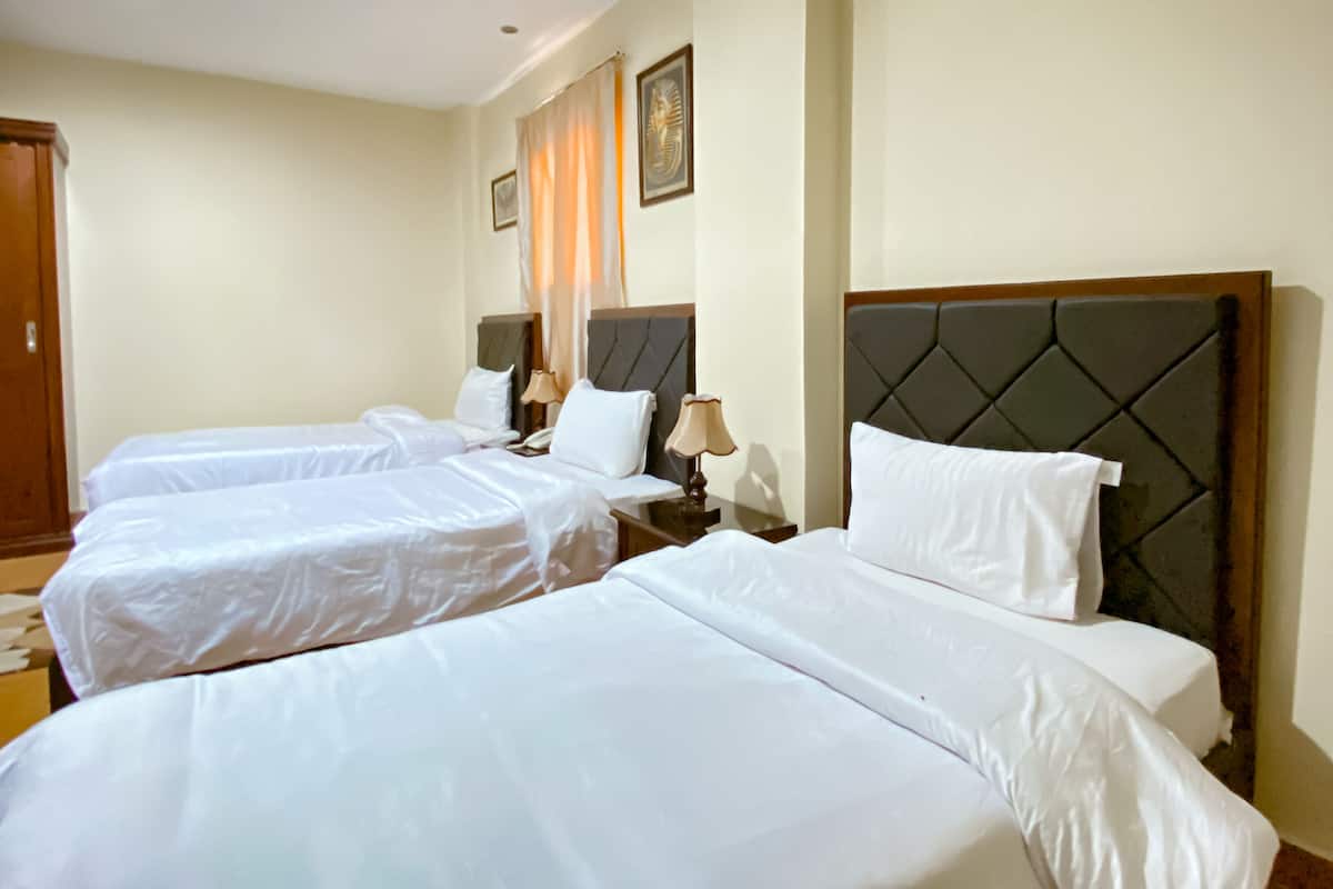 A hotel room with three neatly made beds, each with white linens and headboards. There are bedside tables with lamps and a framed picture on the wall.