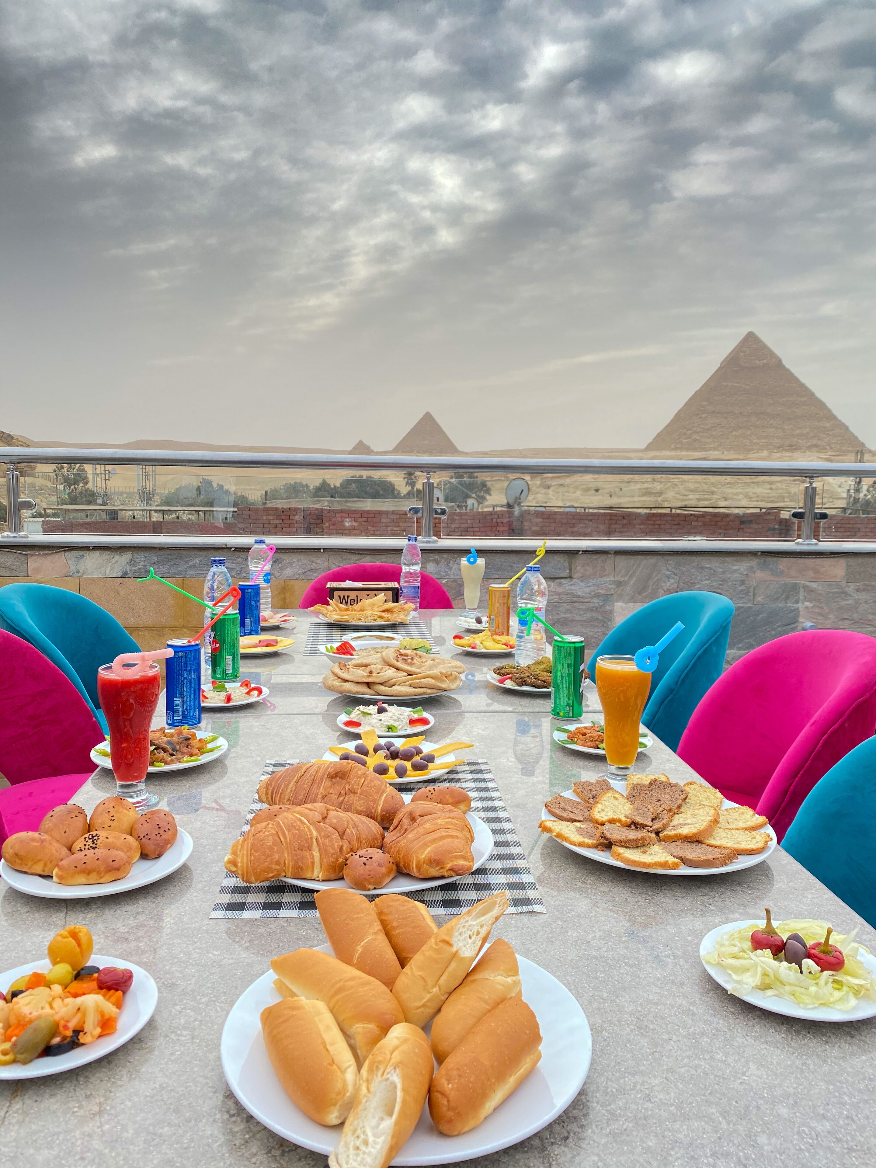 A table set with various foods and drinks, overlooking a pyramid and a desert landscape.