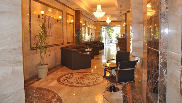 A hotel lobby with a marble floor, sofas, chairs, and a large potted plant.