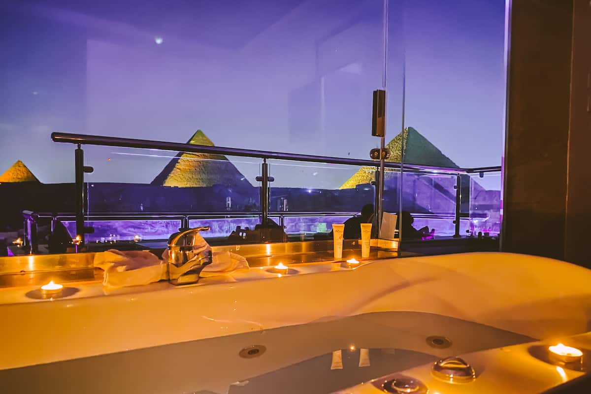 A bathtub with a view of pyramids through a window.