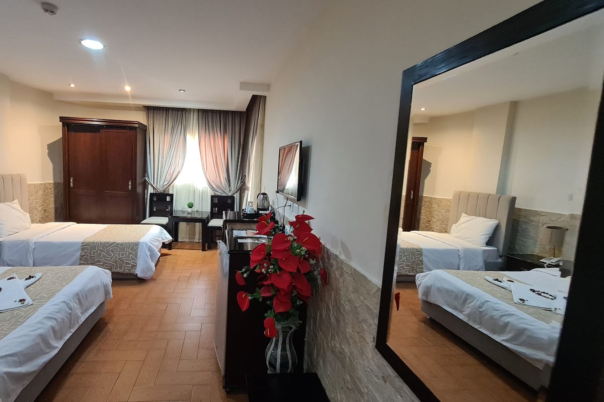 A hotel room with two beds, a desk, a chair, a mirror, and a decorative plant.
