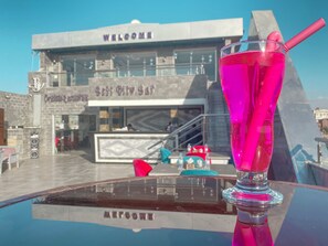 A glass of pink drink on a reflective surface with a 'Welcome' sign and a 'Best City Bar' sign in the background.