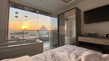Een moderne hotelkamer met een groot bed, een badkamer met bad en uitzicht op de piramide bij zonsondergang.