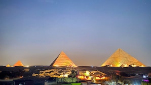 Three illuminated pyramids at night with surrounding infrastructure.