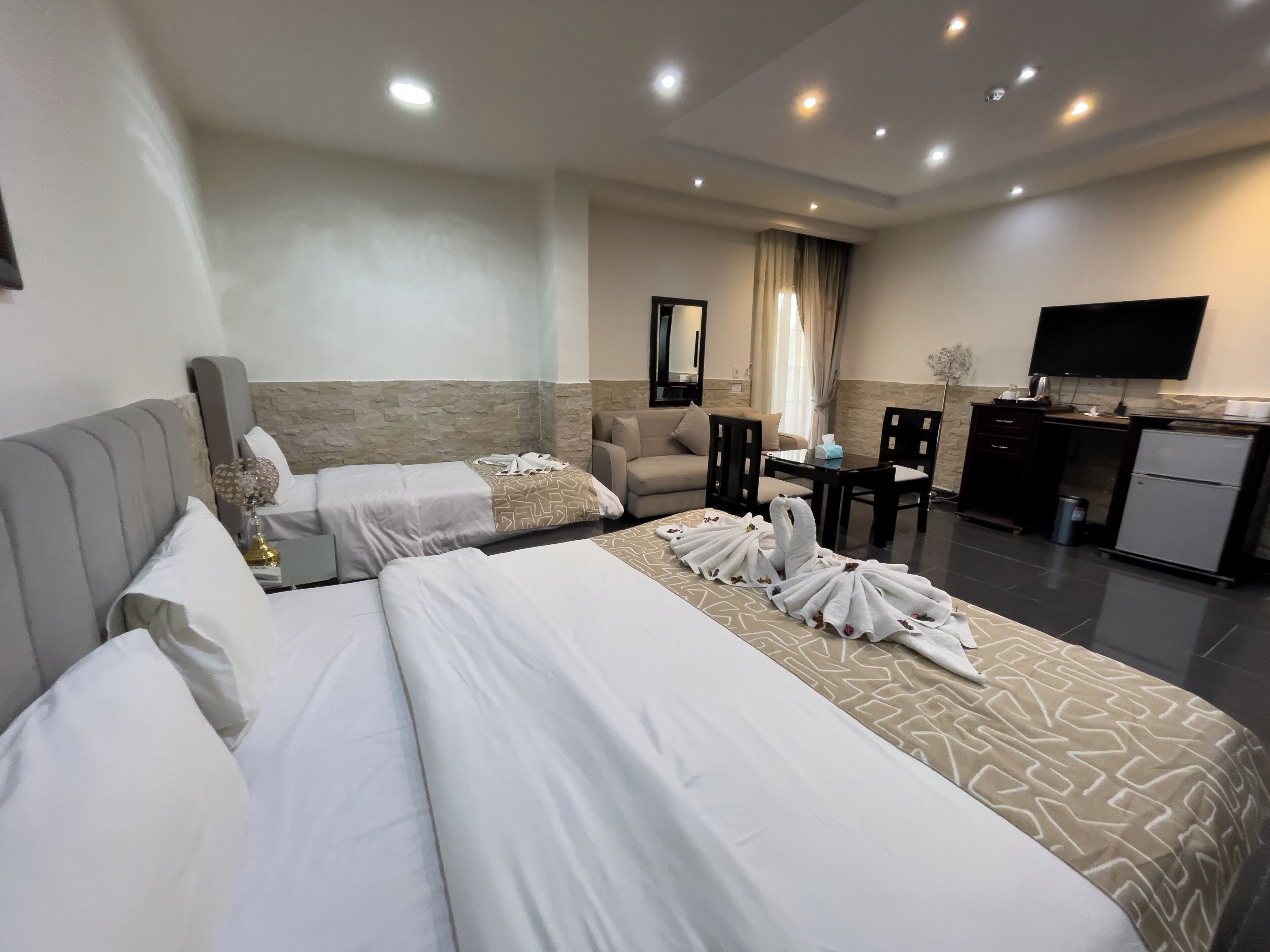 A hotel room with two beds, a sofa, a desk, a television, and a minibar.