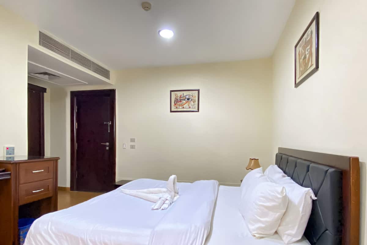 A neatly made bed with white linens and a black headboard, a bedside telephone, and a framed picture on the wall.