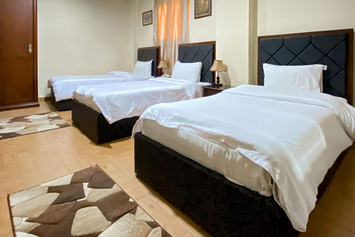 A hotel room with two beds, a wooden wardrobe, a patterned rug, and a framed picture on the wall.