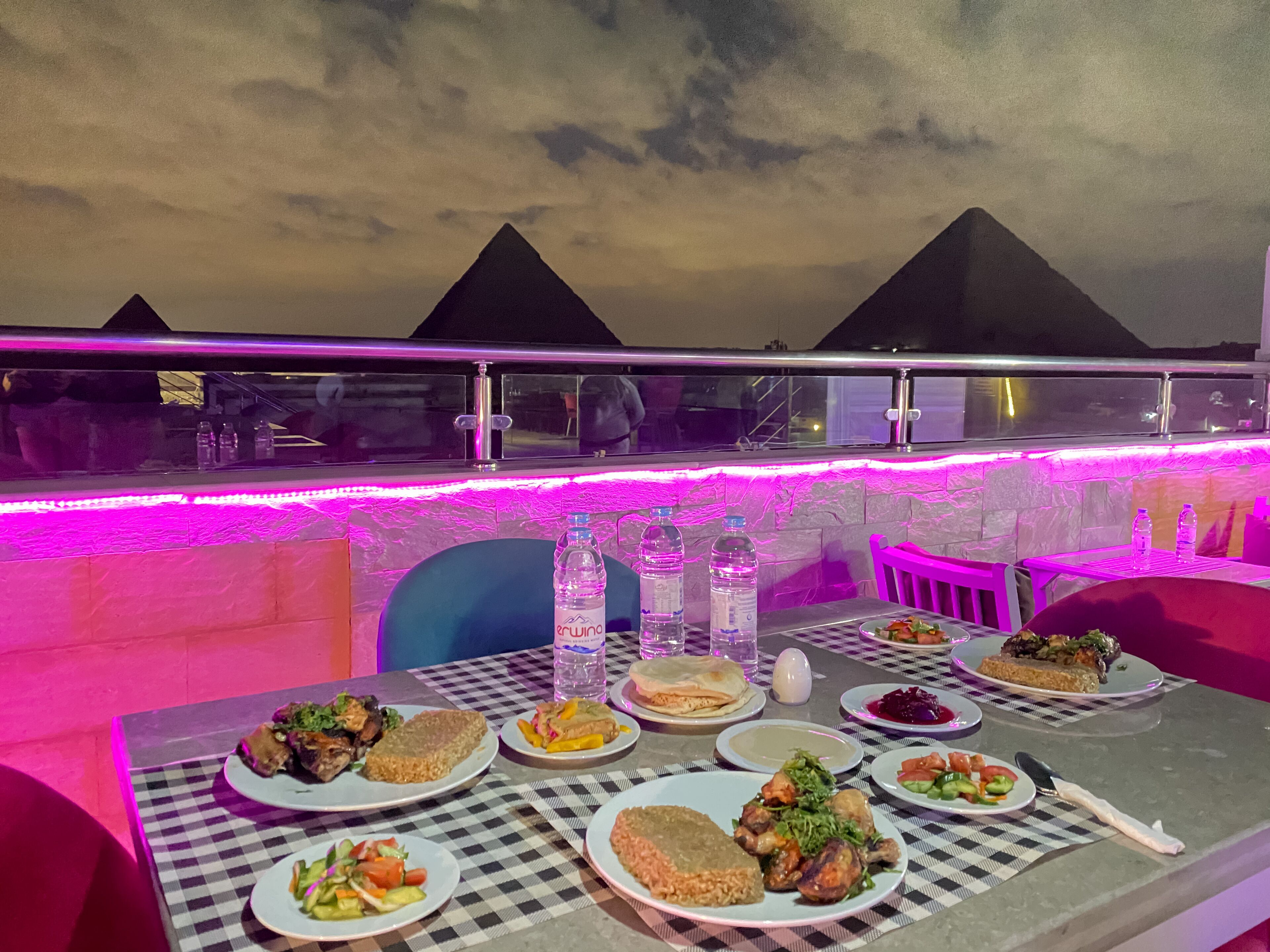 A table set with various dishes and drinks, with a view of pyramids in the background.