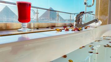 A bathroom with a sink, a glass of red drink, and a window with a view of pyramids.