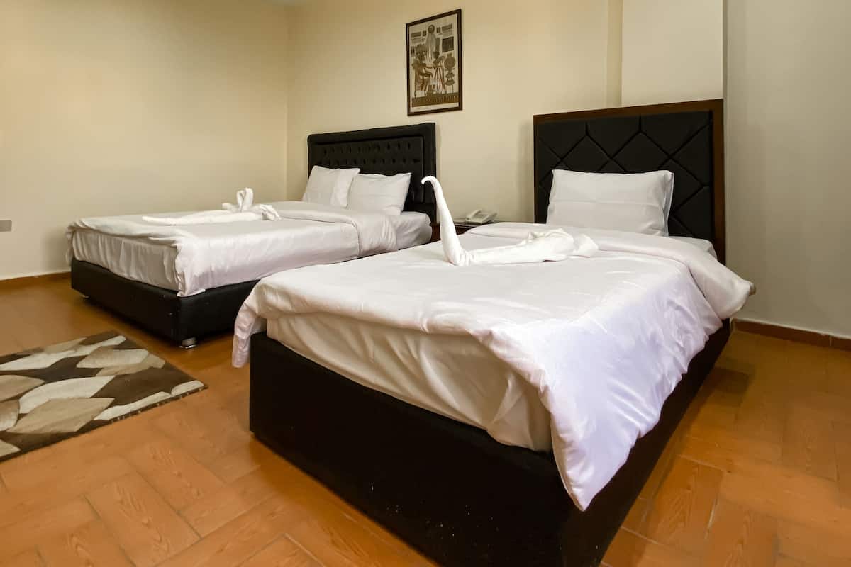 A hotel room with two beds, a wooden floor, and a painting on the wall.