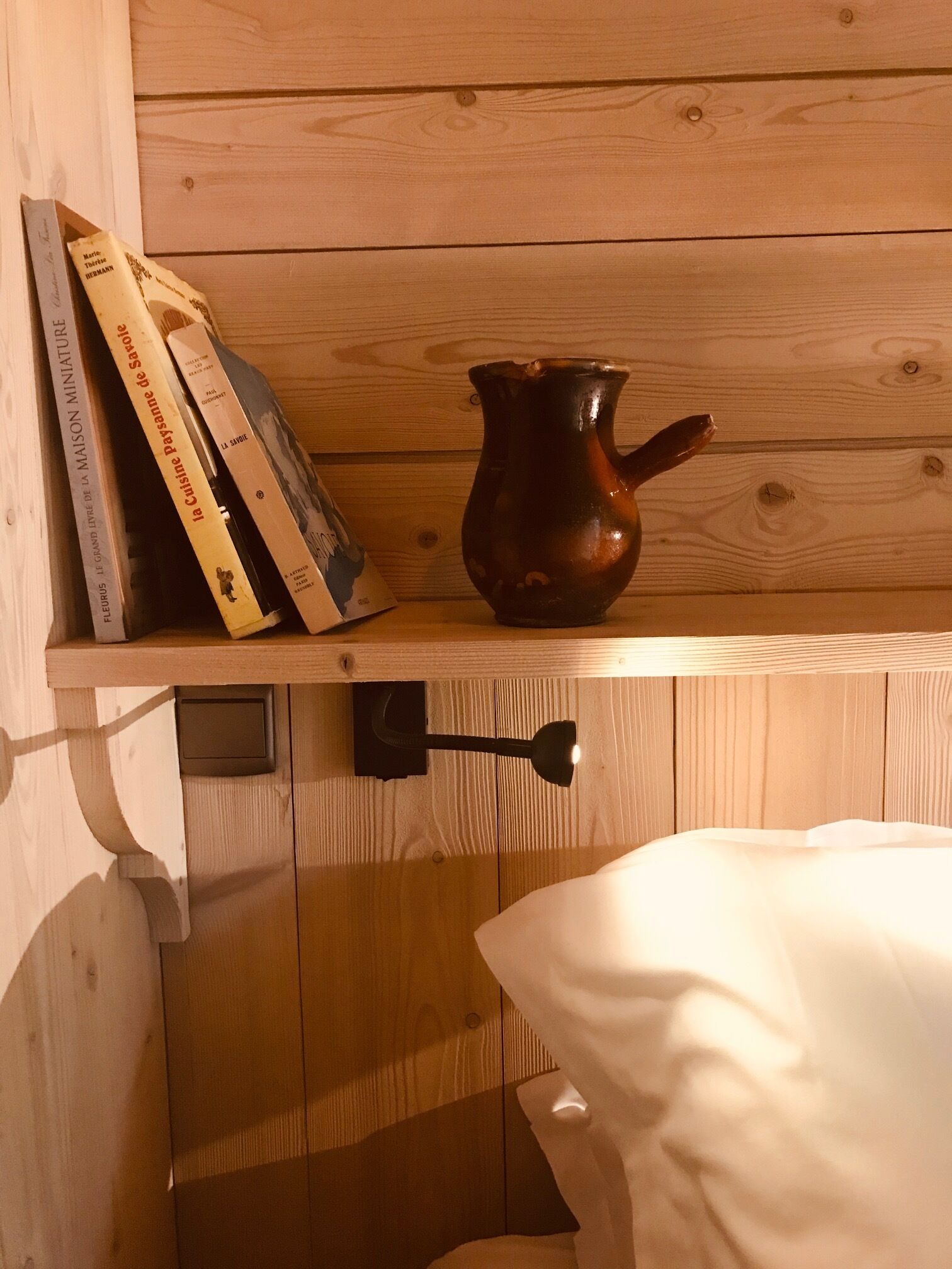 A wooden shelf with books and a ceramic pitcher.