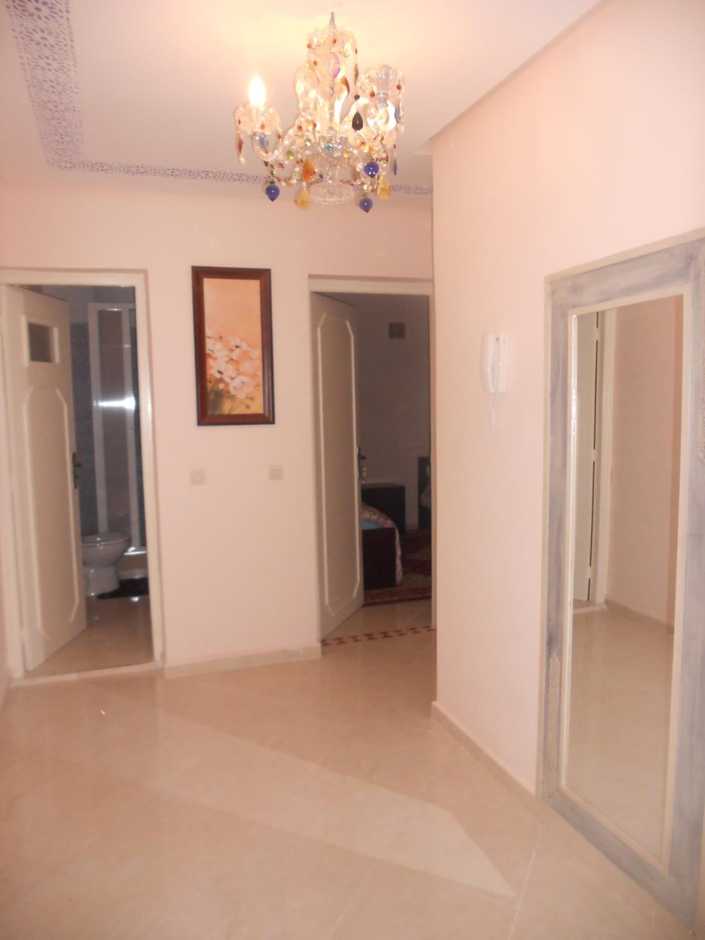 A hallway with a chandelier, a framed picture on the wall, and doors leading to other rooms.