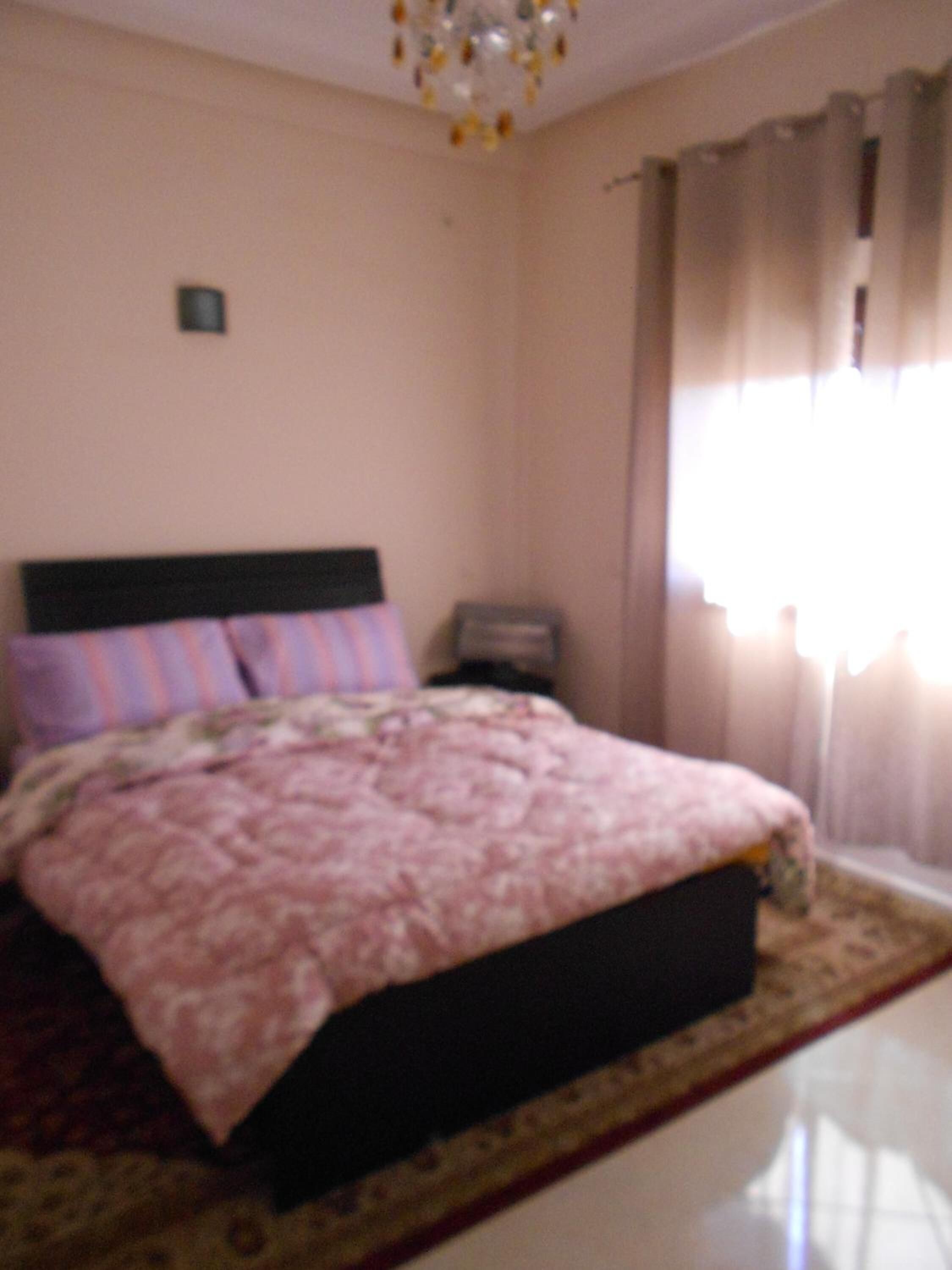 Un dormitorio con cama, mesita de noche y ventana con cortinas.