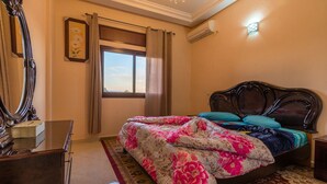 Un dormitorio con una cama grande, un tocador, un espejo, una ventana con cortinas y un equipo de aire acondicionado.