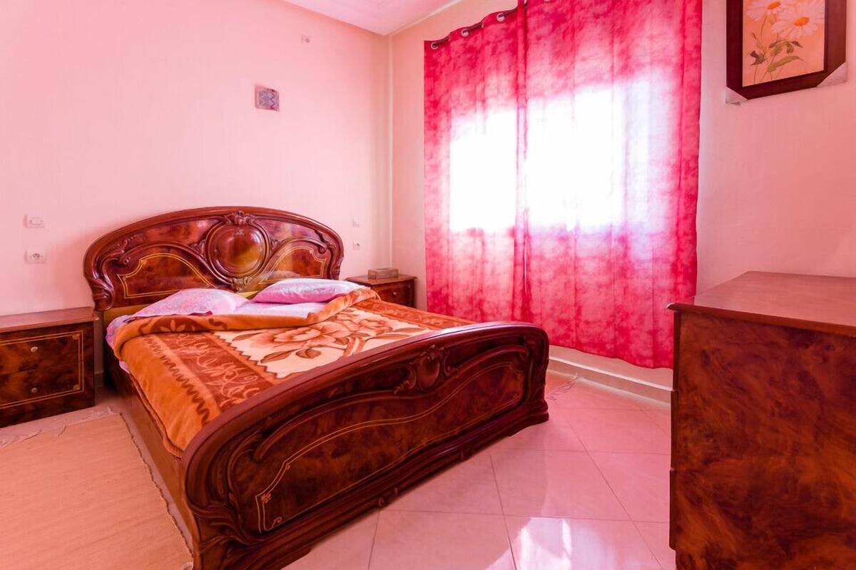 A bedroom with a wooden bed, a nightstand, a dresser, and a window with red curtains.