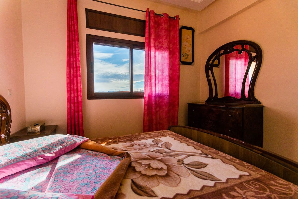 A bedroom with a bed, a window, a mirror, and a dresser.