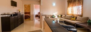A living room with a sofa, a coffee table, and a TV mounted on the wall. - Residence Bab El Janoub (Ouarzazate)
