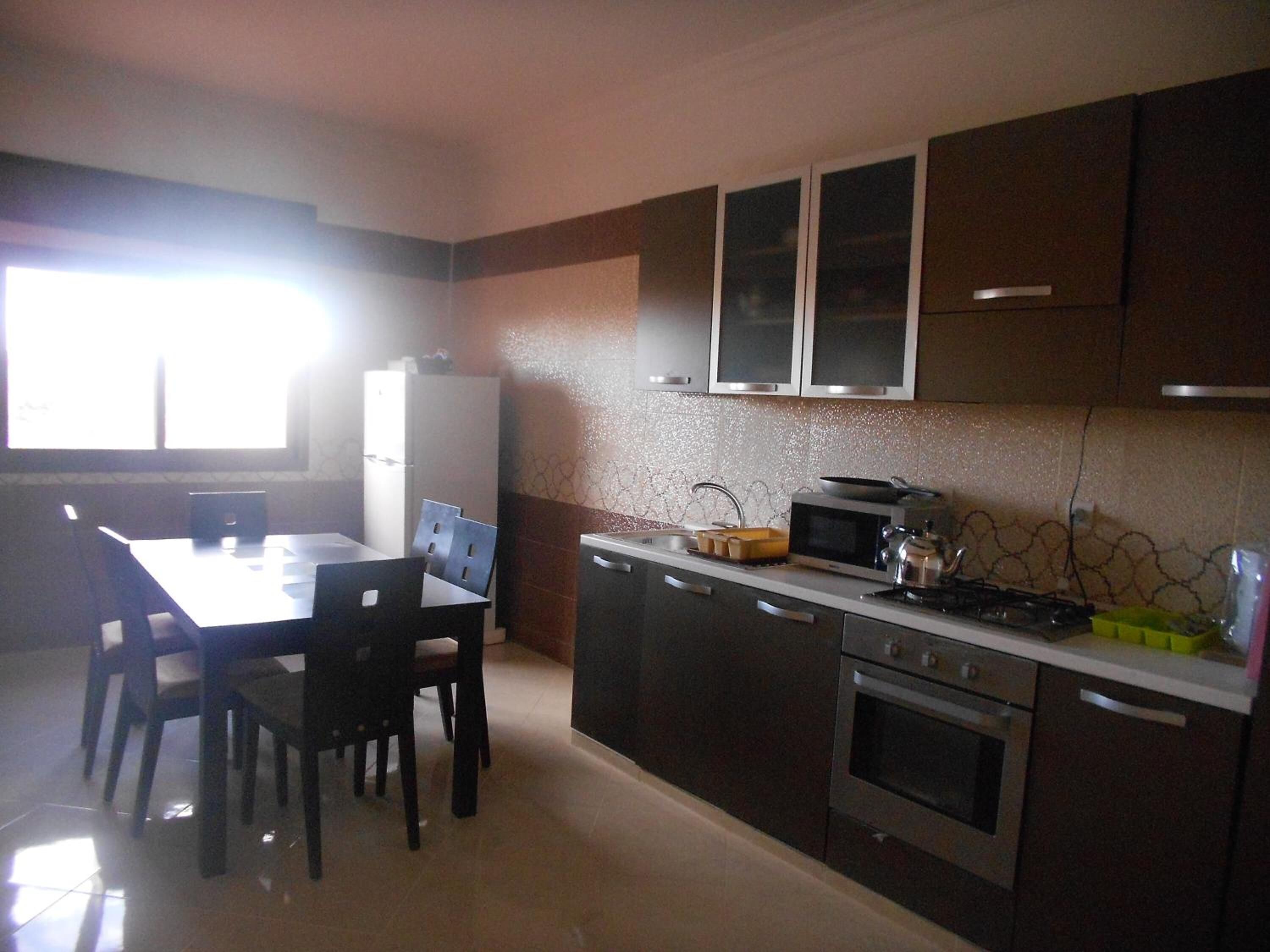 A kitchen with a dining table and chairs, a refrigerator, a microwave, a stove, and cabinets.