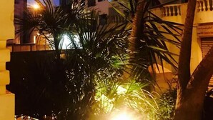 Un edificio de varios pisos con balcones, rodeado de palmeras e iluminado por farolas.