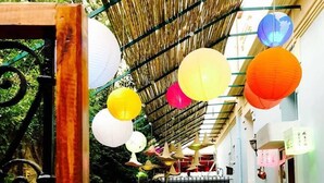 Un comedor interior con mesas y sillas, techo de bambú y faroles de papel colgantes.