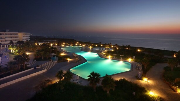 Un complexe hôtelier doté d’une grande piscine illuminée, d’un accès direct à la plage et d’un bâtiment agrémenté de nombreux balcons.