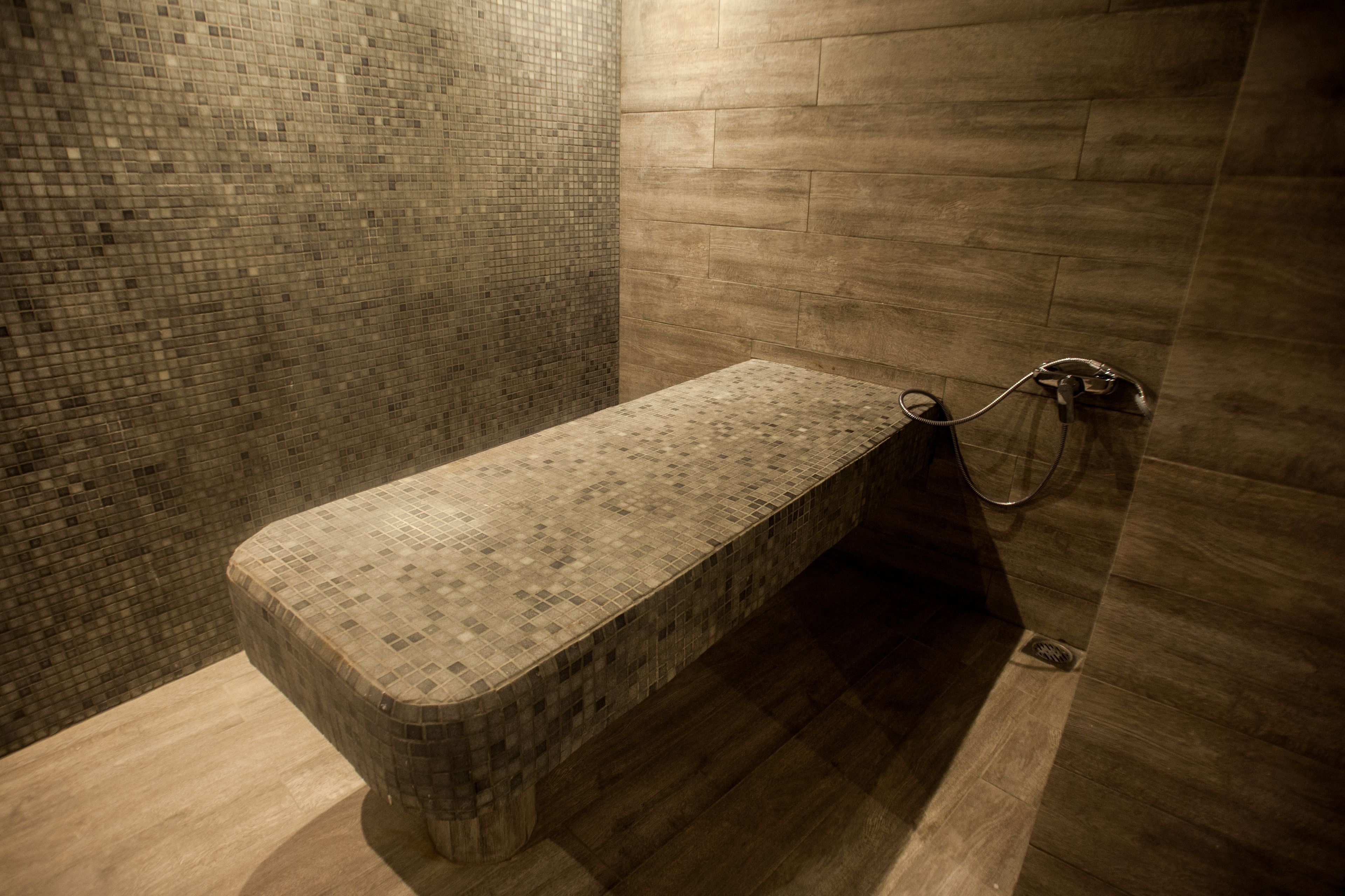 Un espace douche avec un banc carrelé et un pommeau de douche.