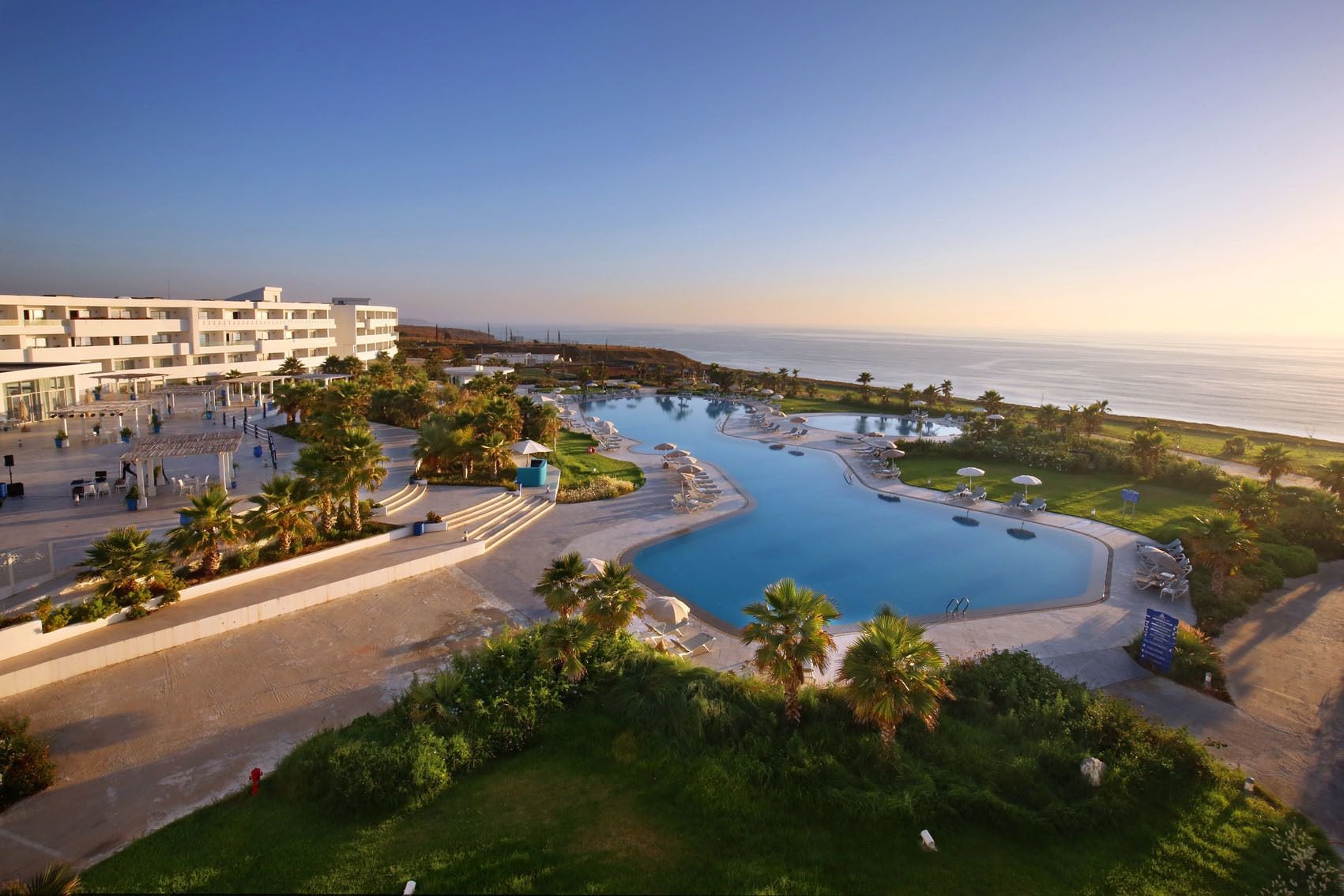 Een resort met een groot zwembad, palmbomen en uitzicht op de oceaan.