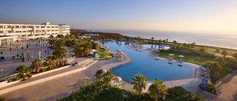 A resort with a large pool, palm trees, and a view of the ocean.