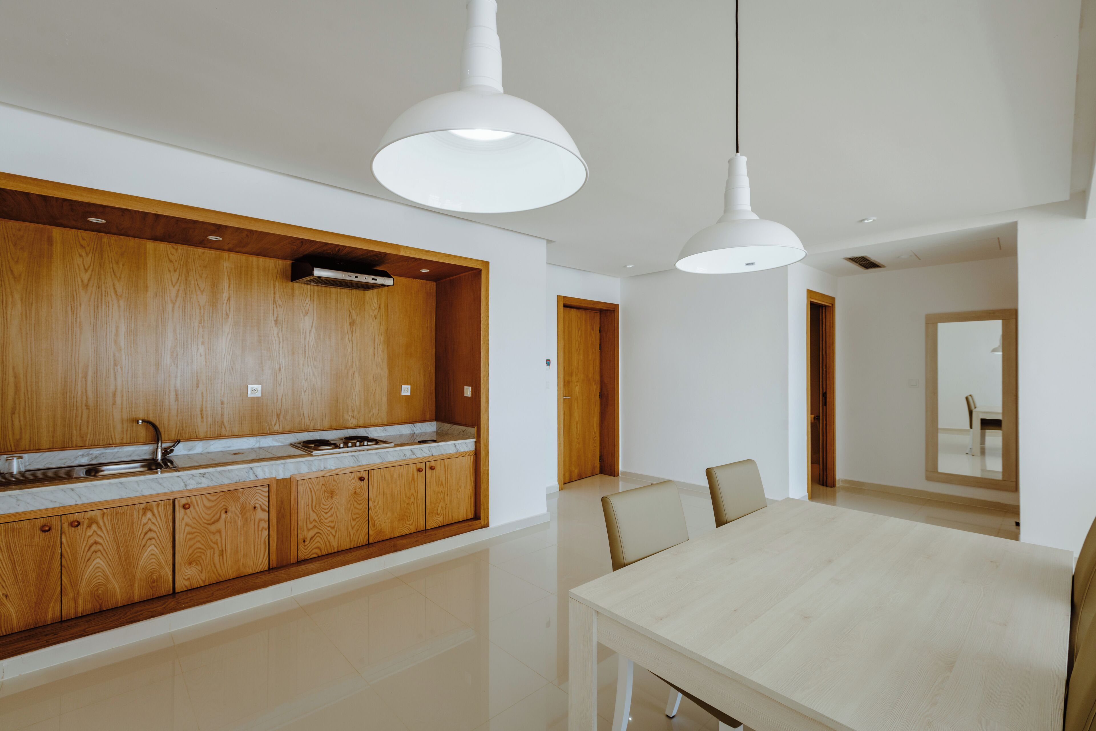 Una cucina moderna con mobili in legno e un piano di lavoro in marmo, una zona pranzo con tavolo e sedie dai toni chiari e illuminazione a sospensione.