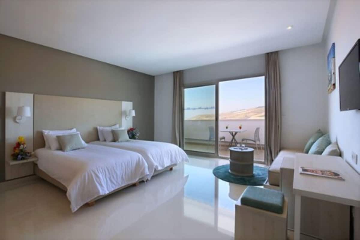 A modern hotel room with a large bed, a desk, and a balcony with a view.