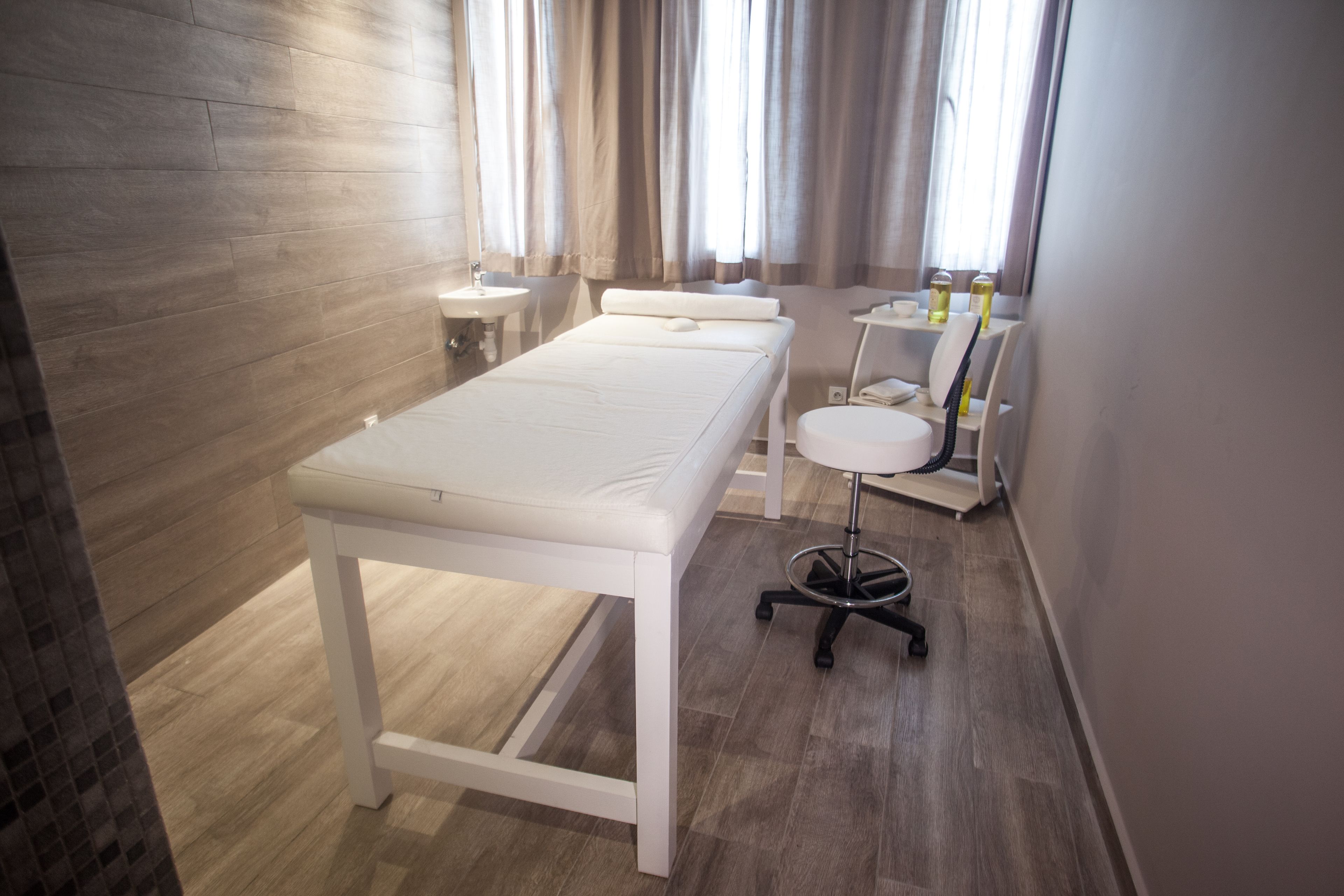 Une chambre propre et moderne, avec un plancher en bois, un lit blanc, une petite table ronde et une chaise.