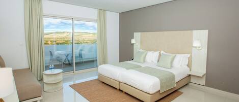 Een moderne hotelkamer met een groot bed, een klein bijzettafeltje, een bank en een balkon met een glazen deur.