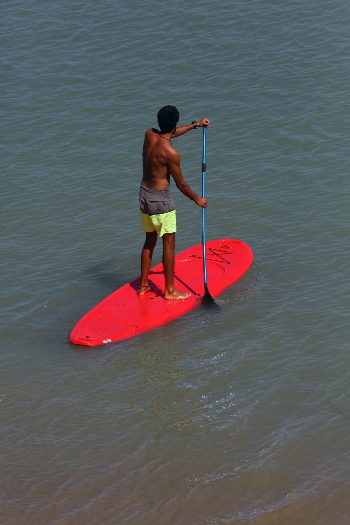 Une personne debout sur une planche de paddle rouge, dans l’eau.