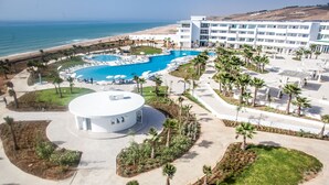 Vue aérienne d’un complexe hôtelier doté d’une grande piscine, de palmiers et d’une plage.