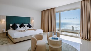 Une chambre d’hôtel avec un lit, deux chaises, une petite table, une vue sur la mer et un balcon.