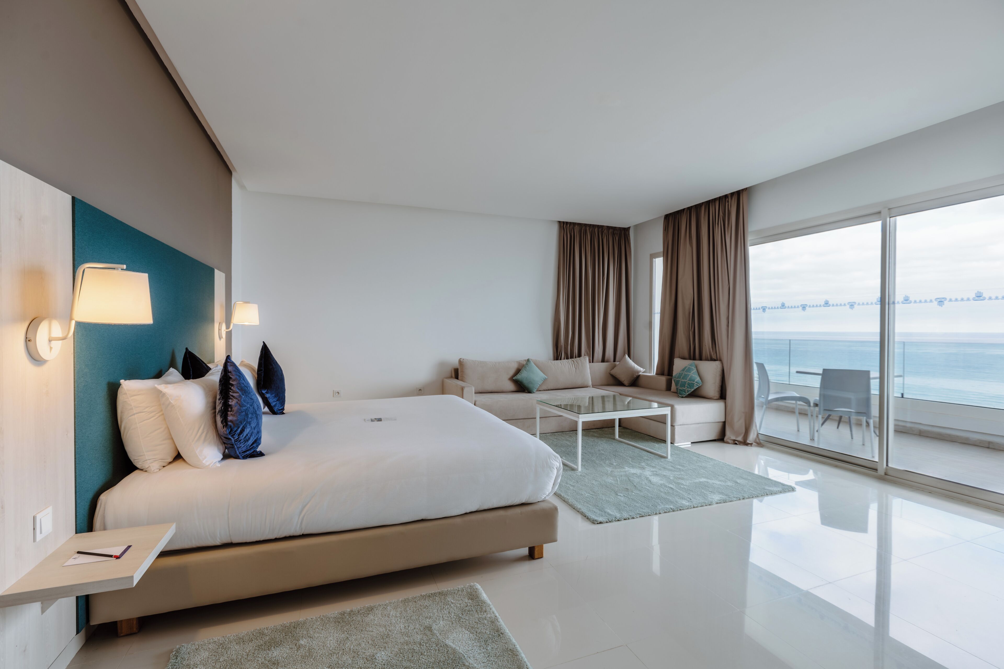 A modern hotel room with a bed, sofa, and a balcony with a view.