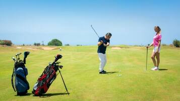 Un parcours de golf comprenant un green d’entraînement, un bunker de sable et un sac de golf.