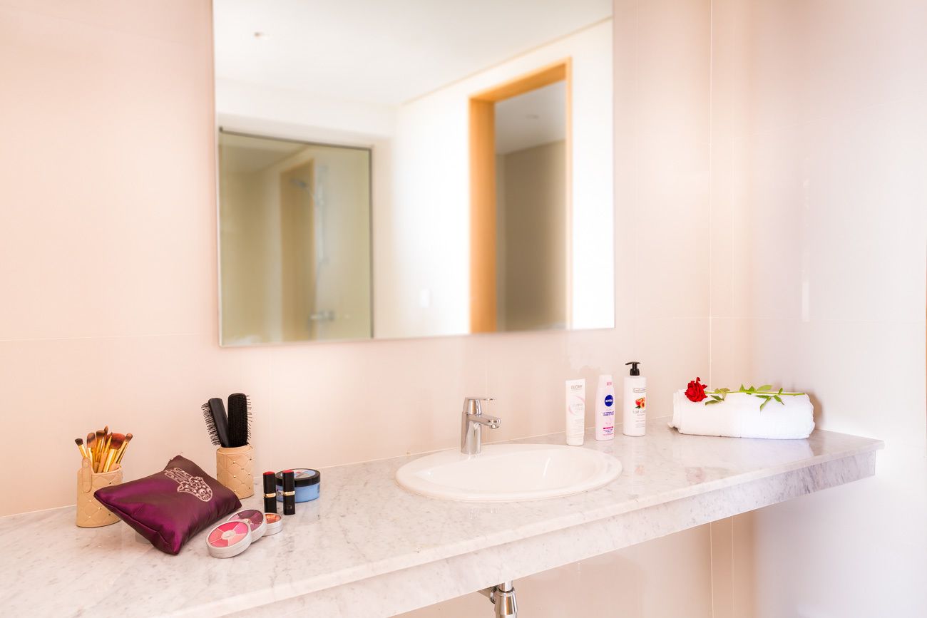 A bathroom with a white sink, a large mirror, and toiletries on the counter.