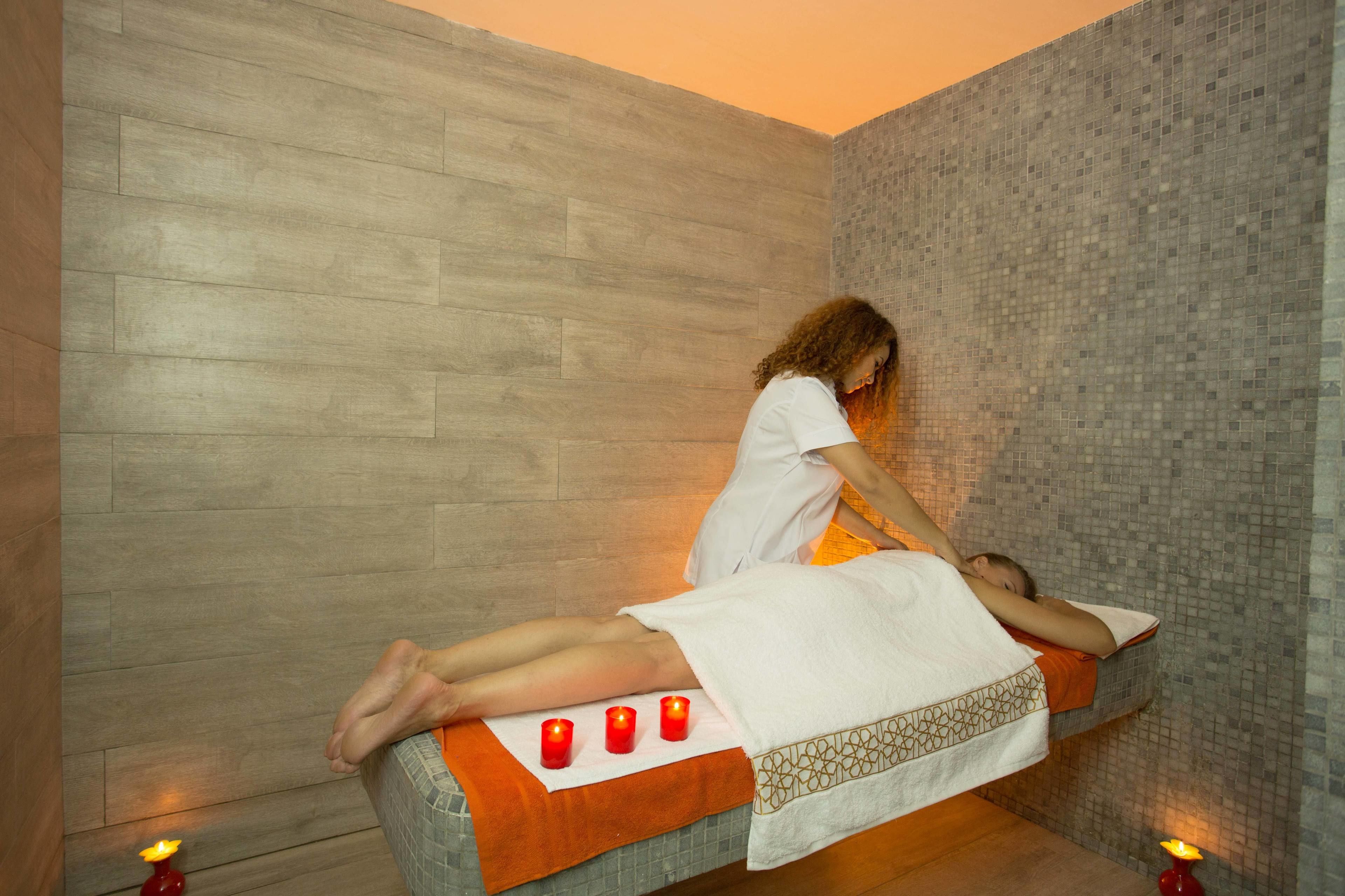 A massage therapy room with a wooden floor, a tiled wall, and a massage table with candles.