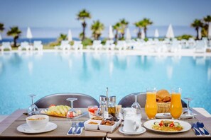 A dining table with breakfast items and drinks by a poolside with a view of the ocean. - Lixus Beach Resort – All Inclusive (Larache)
