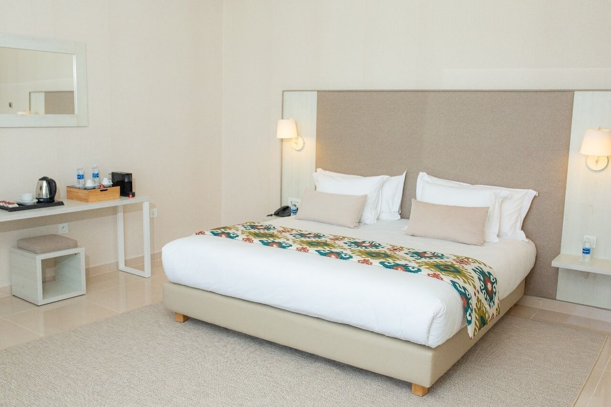 A hotel room with a large bed, a bedside table, a desk, and a mirror.