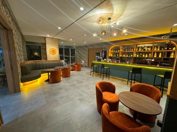 Zona de bar con disposición de asientos, barra y exhibición de botellas.