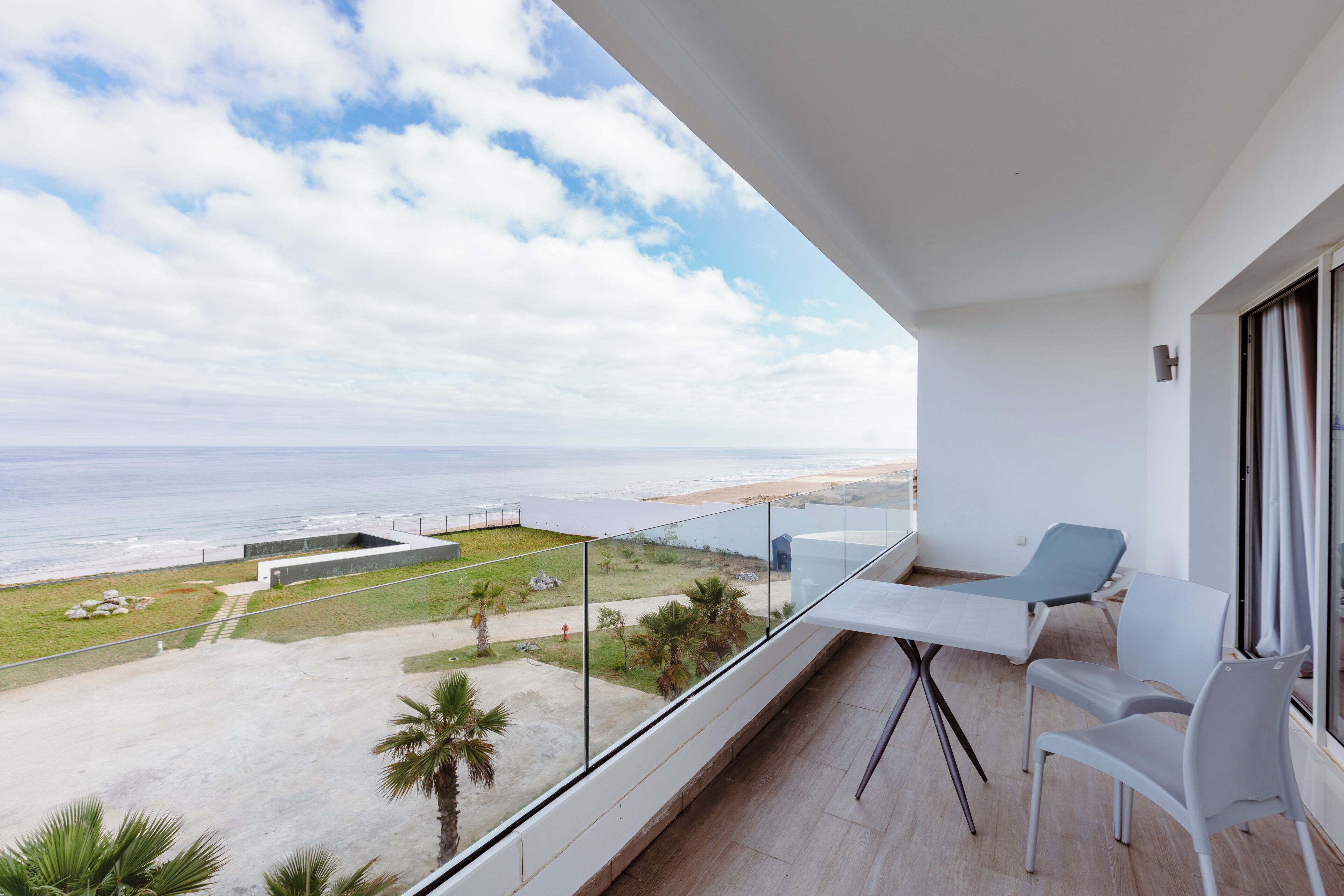 A balcony with a table and chairs, overlooking a beach and ocean.