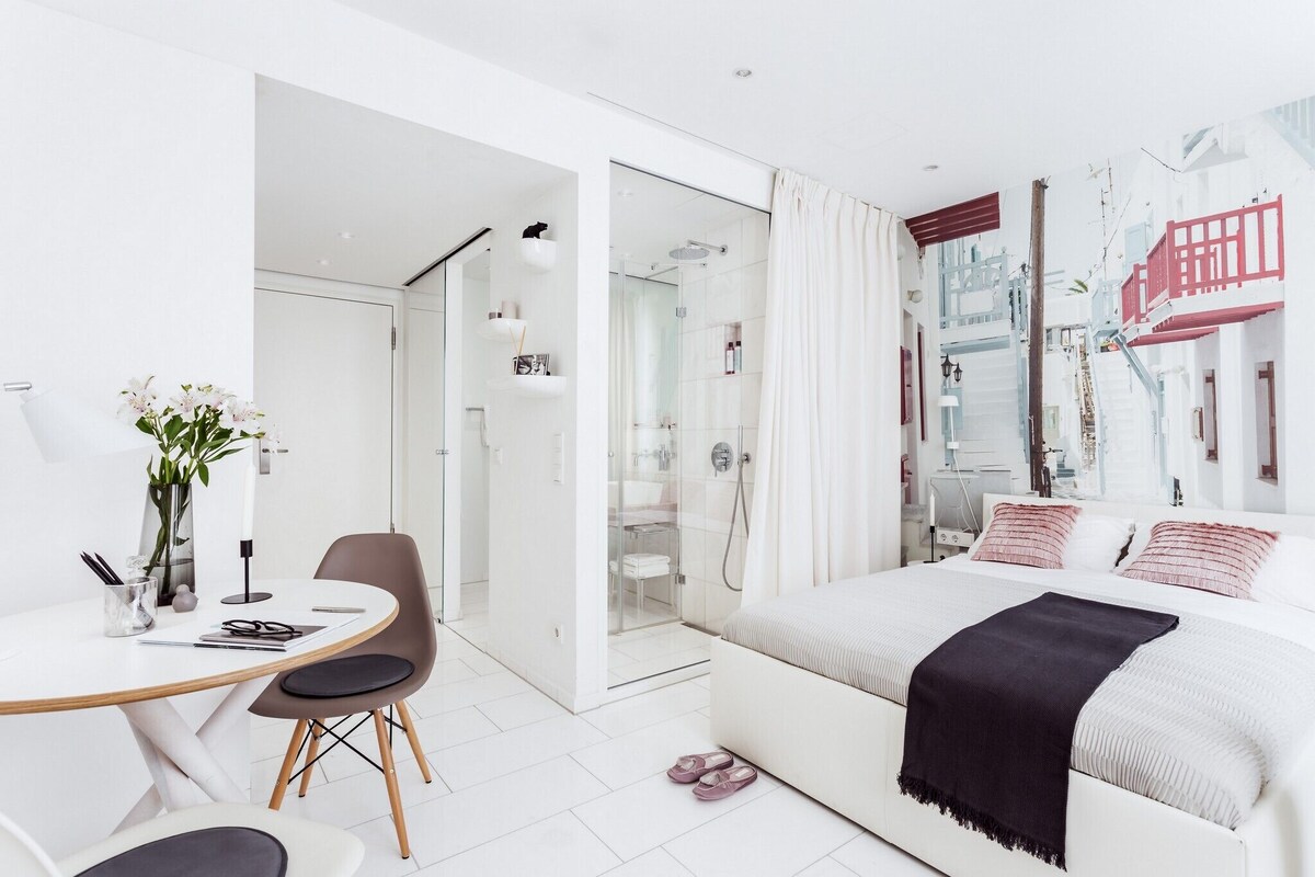 A modern bedroom with a bed, a desk, and a shower area.