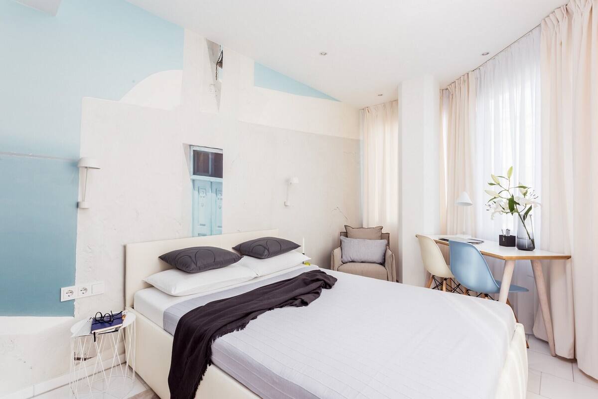Una habitación de hotel moderna con cama, mesita de noche, silla, escritorio y cortinas.