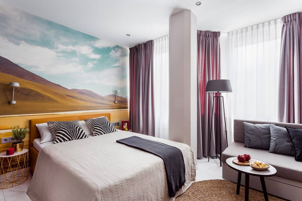 Una habitación de hotel con una cama grande, un sofá, una mesita con fruta y un cuadro de un paisaje desértico.
