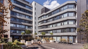 A modern multi-story building with a courtyard featuring benches and potted plants. - Skyreach Bizzstay - Wohnen Am Main (Frankfurt)